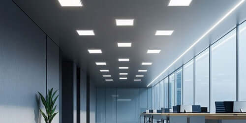 Modern office space illuminated by sleek downlights and LED panels, featuring large windows and minimalistic design.